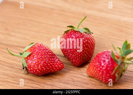 Fraise. Trois baies fraîches et crues sur fond de bois. Banque D'Images