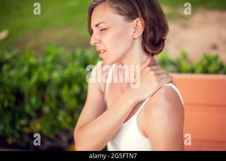 Douleurs au cou. Femme qui ressent une douleur au cou ou à l'épaule à l'extérieur. Concept de soins de santé et de mode de vie Banque D'Images