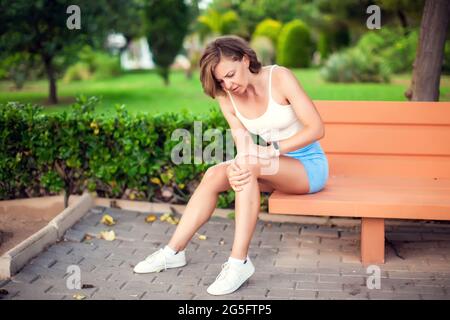 Douleurs au genou. Femme atteinte de genoux assise sur le banc à l'extérieur. Concept de soins de santé et de mode de vie Banque D'Images