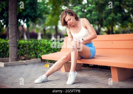 Douleurs au genou. Femme atteinte de genoux assise sur le banc à l'extérieur. Concept de soins de santé et de mode de vie Banque D'Images