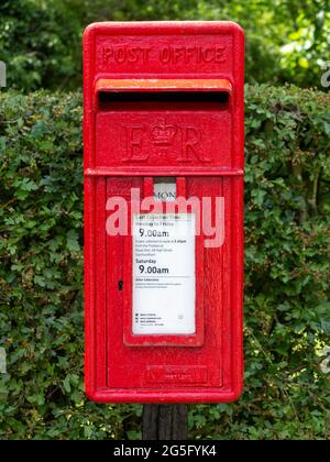 Boîte aux lettres de bureau de poste en fonte rouge montée sur un poteau devant une haie Banque D'Images