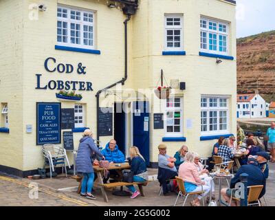 Une foule de personnes qui mangent à l'extérieur du pub Cod and Lobster sur le front du port de Staithes North Yorkshire en été Banque D'Images