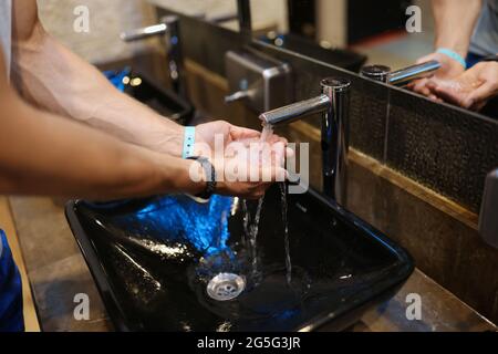 Homme se lavant les mains sous l'eau courante du robinet dans les toilettes publiques de près Banque D'Images