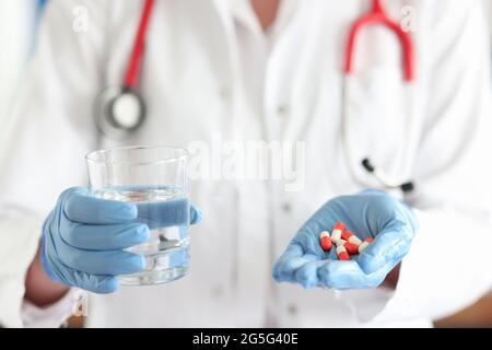 Médecin tenant un verre d'eau et des capsules médicales dans ses mains de près Banque D'Images