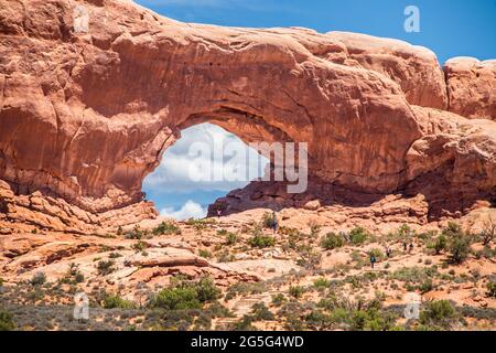 Immense arche rouge naturelle au parc national d'Arches, dans l'Utah, aux États-Unis, avec des touristes qui marchent dans les escaliers de roche vers elle. Banque D'Images