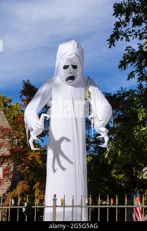 Fantôme blanc géant effrayant - zombie explosion Halloween décoration tours au-dessus de la maison entouré d'arbres d'automne avec des griffes prêtes à attaquer derrière la clôture avec l'esprit Banque D'Images