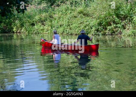 Couple en canoë deux hommes, pagayant le long de la rivière. Banque D'Images