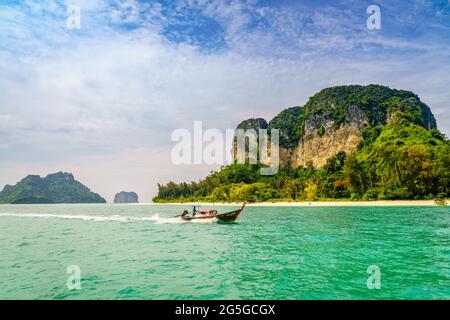 Bateau thaïlandais à longue queue qui passe devant une plage sur une île au large de la côte de Krabi, dans la mer d'Andaman, en Thaïlande Banque D'Images