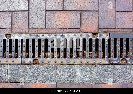 une grille de drainage en fer d'un chenal de pluie sur un trottoir piétonnier fait de carreaux de pierre l'aménagement paysager urbain de l'infrastructure des parcs. Banque D'Images