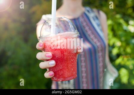 Femme main tenant l'eau de glace rouge dans une tasse en plastique. Boisson glacée - boisson fraîche et saine d'été ou cocktail. Journée ensoleillée Banque D'Images