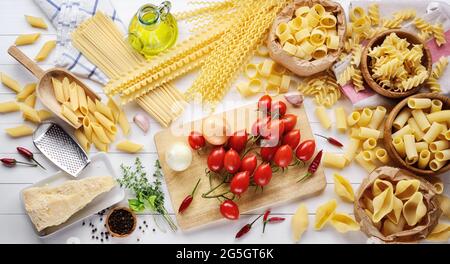 Pâtes et ingrédients : tomates, parmigiano, huile d'olive extra vierge, penne, coquilles, rigatoni, mafalda, linguine, fusilli et calmar sur bac en bois blanc Banque D'Images