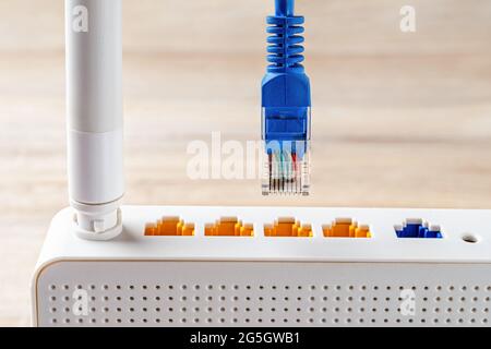 La fiche du câble réseau bleu macro est presque insérée dans la prise jaune du routeur sans fil Wi-fi blanc. Routeur WLAN pour Internet domestique et professionnel. Banque D'Images