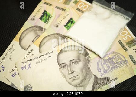 Argent et un sac de poudre blanche. Cocaïne dans un sac en plastique sur fond noir, gros plan. L'argent ukrainien, la hryvnia et la drogue sur la table Banque D'Images