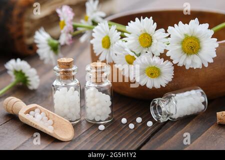 Flacons de granules d'homéopathie. Remède homéopathique - Chamomilla. Pâquerettes fleurs dans un bol en bois. Concept de médecine d'homéopathie. Banque D'Images