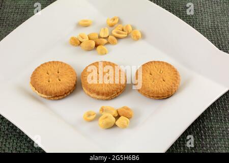 Biscuits sandwich à la crème d'arachide avec arachides sur une assiette à collation blanche Banque D'Images