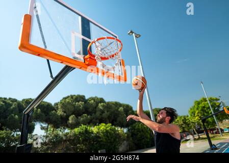 Un sportif masculin jouant au basket-ball lance le ballon sur le terrain de jeu, faisant avec succès la vue de dunk de derrière. Prise de vue de précision Banque D'Images