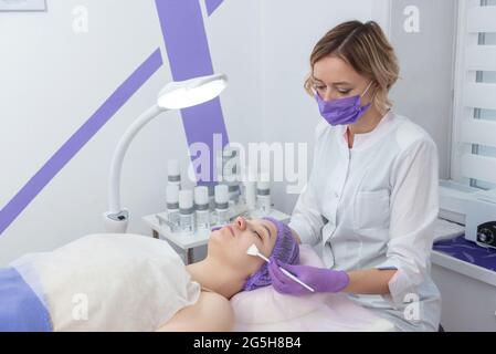 Traitement au rétinol par brosse pour le visage. Procédure de gommage de la femme de beauté. Cosmétologie thérapie jeune fille.acide hyaluronique. Banque D'Images