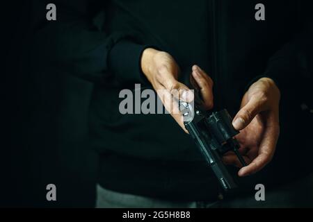 Recharger le revolver gros plan. Les mains des hommes vérifient la présence de balles dans le canon. Guy en Jean et sweat à capuche noir prépare le pistolet pour les coups. Arme à feu pour la défense ou l'attaque. Copier l'espace pour le texte. Banque D'Images