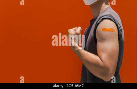 Vaccinations, pansement sur le concept de bras des personnes vaccinées. Bandage adhésif de couleur orange sur le bras de l'homme fort qui fiste la main et montrant le musc Banque D'Images
