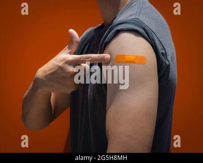 Vaccinations, pansement sur le concept de bras des personnes vaccinées. Bande adhésive de couleur orange sur le bras de l'homme fort qui pointe son propre épaule vers l'avant Banque D'Images