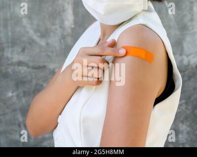 Vaccinations, pansement sur le concept de bras des personnes vaccinées. Bande adhésive de couleur orange sur le bras de la femme d'affaires qui porte un masque blanc, p Banque D'Images