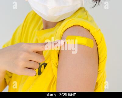 Vaccinations, pansement sur le concept de bras des femmes vaccinées. Main pointant sur le bandage adhésif jaune sur son épaule qui porte une chemise jaune, wh Banque D'Images