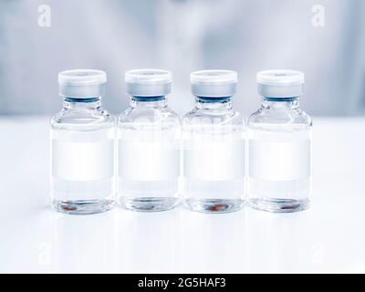 Flacons de vaccins médicaux avec une étiquette blanche sur la table blanche. Image en gros plan de quatre flacons de vaccin en verre pour injection. Banque D'Images