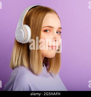Confiante jeune femme dans le portrait de casque. Belle femme sérieuse avec la coiffure blonde appréciez écouter la musique de chanson dans le casque isolé au-dessus de violet Banque D'Images