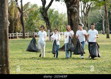 De jeunes volontaires positifs transportant des sacs de déchets qu'ils ont ramassés sur le campus ou dans le parc de la ville Banque D'Images