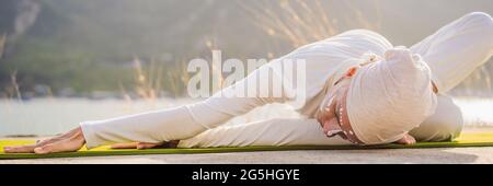 BANNER, LONG FORMAT Kundalini yoga femme en vêtements blancs et le turban pratique le yoga kundalini sur le fond de la mer, les montagnes et le coucher du soleil Banque D'Images