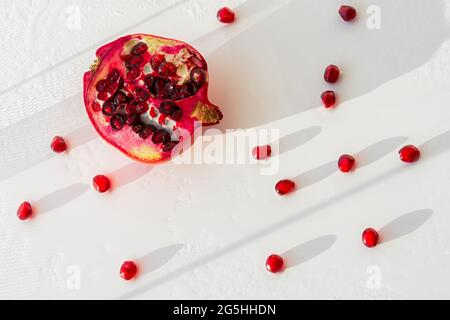 Fruits de grenade aux grains épars sur fond blanc vue de dessus. Une composition authentique dans la lumière du soleil et les ombres. Gouttelettes d'eau sur les graines. Banque D'Images