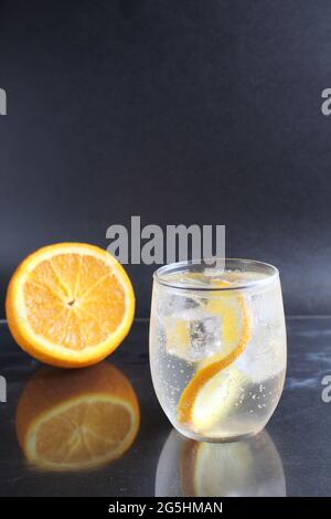 limonade à l'orange et à la glace dans un verre sur fond noir à côté de la glace et de l'orange. Boisson d'été sur fond noir. Banque D'Images