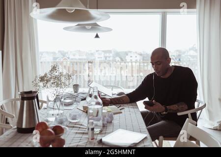 Professionnel hispanique de sexe masculin utilisant un téléphone portable assis à une table dans le salon Banque D'Images