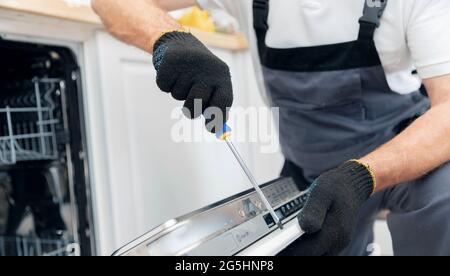 Réparation en gros plan et installation du lave-vaisselle, ouvrier masculin avec l'outil en uniforme. Banque D'Images