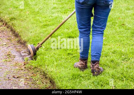 Une femme utilise un coupe-ficelle pour tondre le bord de la pelouse le long de l'allée. Banque D'Images