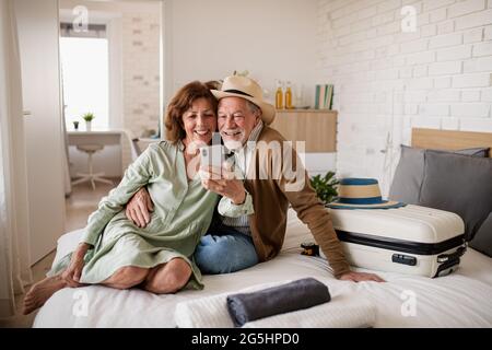 Couple senior heureux avec smartphone dans la chambre d'hôtel, en train de prendre le selfie. Banque D'Images