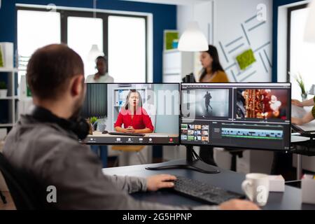 Vidéaste en conférence Web en ligne avec chef de projet sur l'édition de vidéo appel travail client, obtenir des commentaires sur le film commercial en utilisant le logiciel de post-production sur deux moniteurs dans le bureau de démarrage Banque D'Images