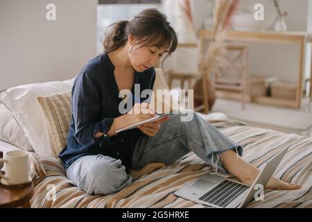 Femme prenant des notes dans un ordinateur portable, travaillant à la maison. Concept de travailleur indépendant, travail à distance, bureau à domicile Banque D'Images
