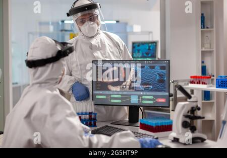 Équipe scientifique dans la combinaison de la prorata discutant du traitement devant le pc regardant le développement de virus. Les médecins d'équipe travaillant avec divers échantillons de bactéries, de tissus et de sang, la recherche pharmaceutique pour les antibiotiques Banque D'Images
