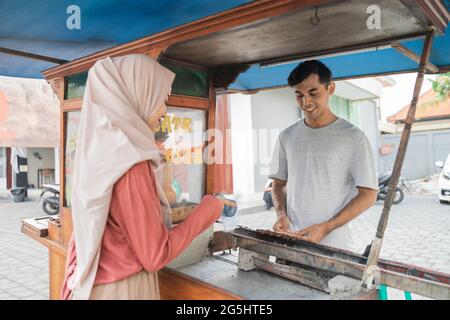 femme musulmane commandant le satay de poulet du vendeur de petit chariot alimentaire. Banque D'Images