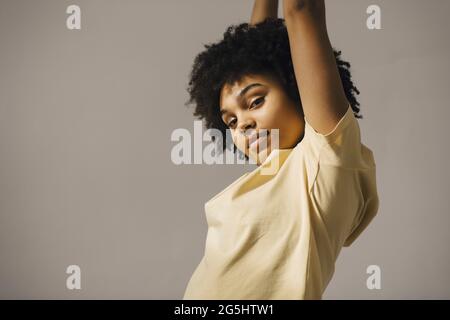 Portrait d'une femme aux cheveux bouclés avec les bras levés sur fond beige Banque D'Images