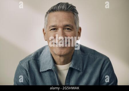 Portrait d'un homme mûr souriant portant une veste bleue contre un mur beige Banque D'Images