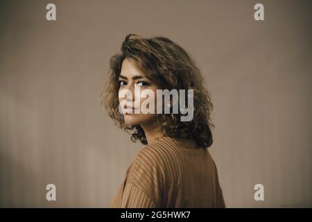 Portrait d'une femme adulte de taille moyenne portant un dessus marron sur fond beige Banque D'Images