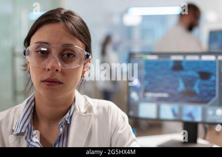 Microbiologiste épuisé avec verre de protection assis en laboratoire regardant la caméra. Chimiste surtravaillé examinant l'évolution du virus en utilisant la haute technologie pour la recherche scientifique, vaccin. Banque D'Images