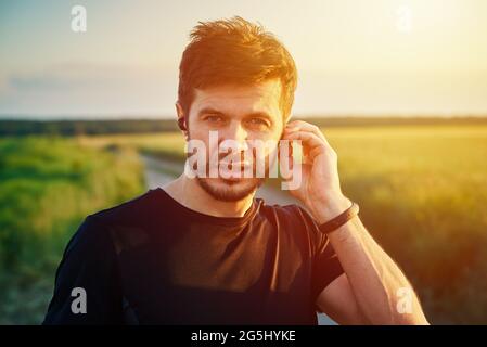 Homme se préparant à courir au coucher du soleil, à allumer les écouteurs sans fil. Portrait de l'homme mlenial actif du caucase Banque D'Images