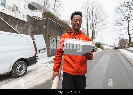 Jeune liveur transportant des colis tout en marchant sur la route Banque D'Images