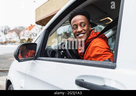 Jeune conducteur souriant regardant en arrière par la fenêtre pendant la conduite de la camionnette Banque D'Images