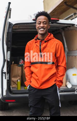 Portrait d'un jeune homme de livraison heureux debout avec les mains dans les poches contre la camionnette Banque D'Images