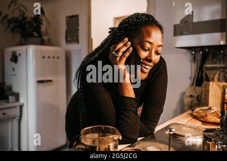Une jeune femme parle avec un smartphone tout en se penchant sur le comptoir de la cuisine Banque D'Images