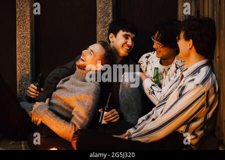 Des amis heureux se rafraîchilant avec des bouteilles de bière tout en étant assis sur le balcon Banque D'Images